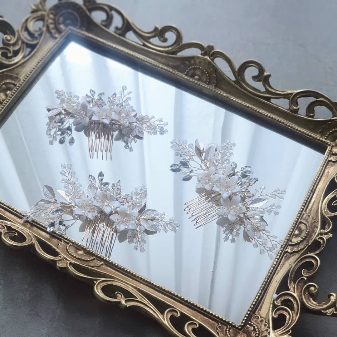 Three decorative bridal hair combs with white flowers and pearls on a gold mirror.