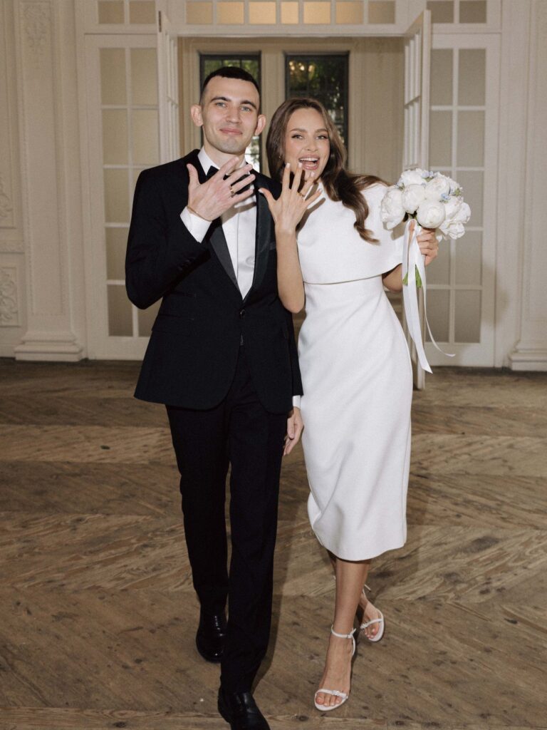 Couple posing in wedding attire, woman wearing a chic midi white wedding dress