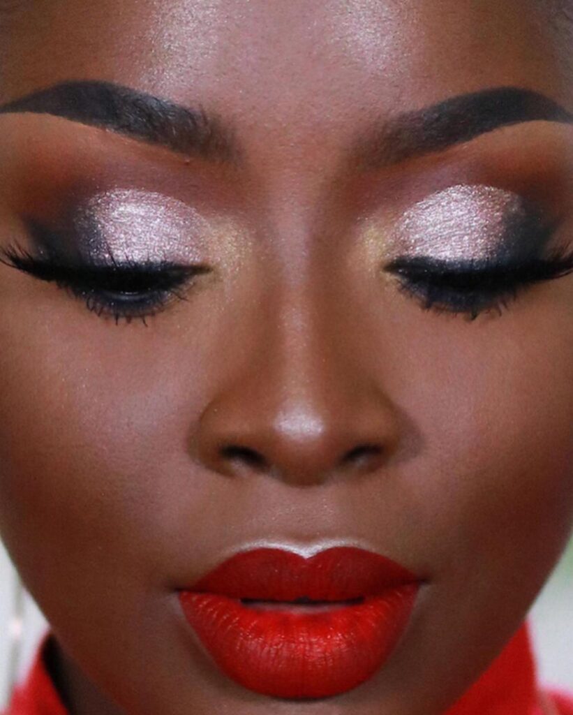 Dark-skinned woman wearing bold red lipstick and shimmering gold eyeshadow with closed eyes.