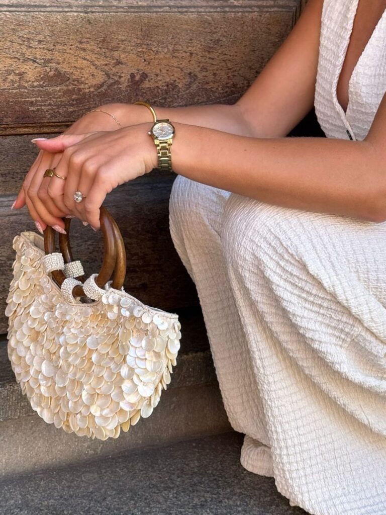 White shell-sequined handbag with wooden handles held by a woman in white dress.