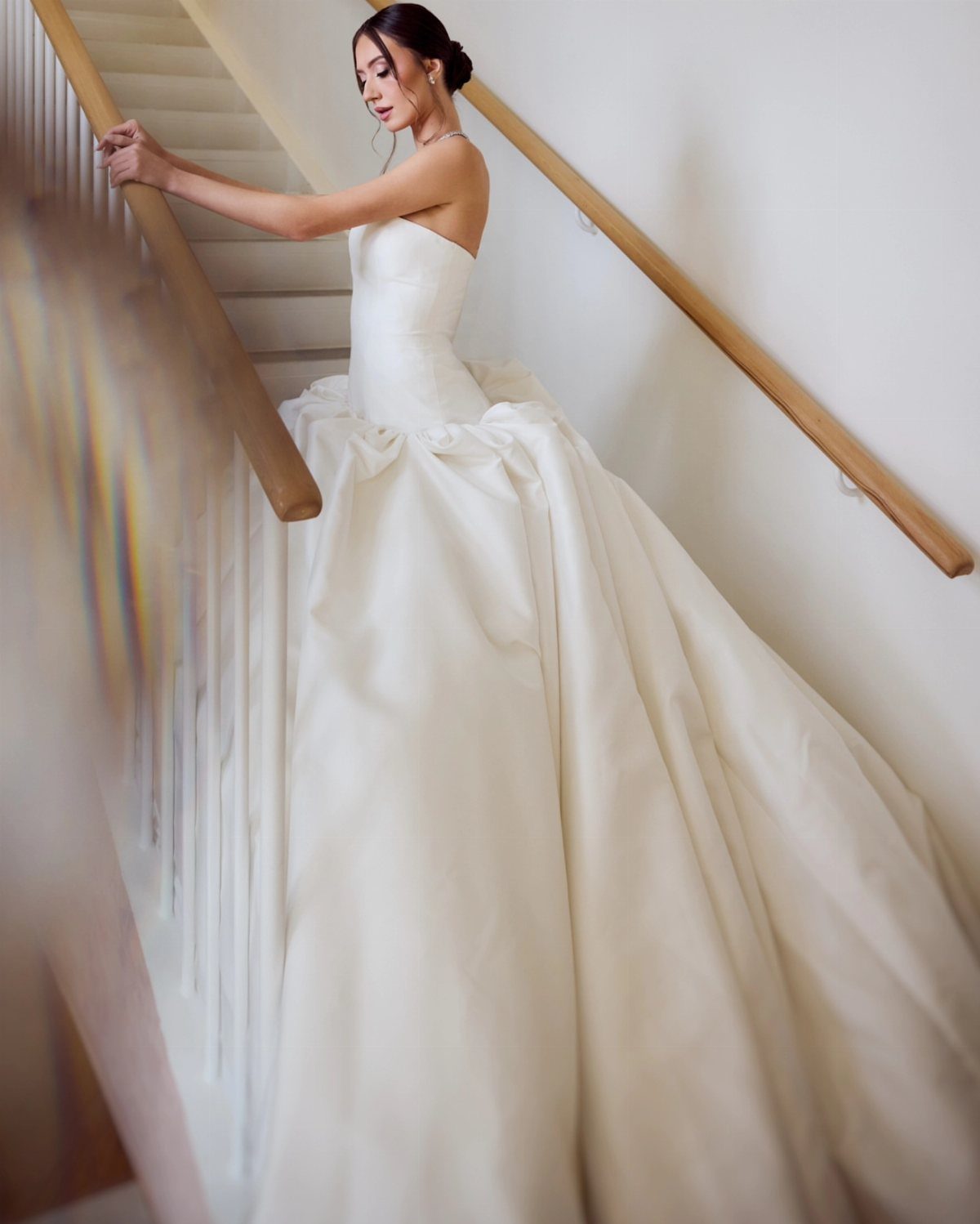 Woman in a strapless white drop waist wedding dress standing on a staircase