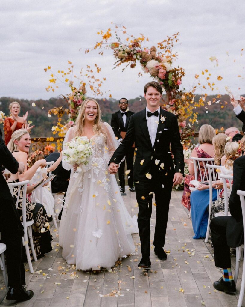 Bride in lace flowy wedding dress and groom walking through falling yellow petals.