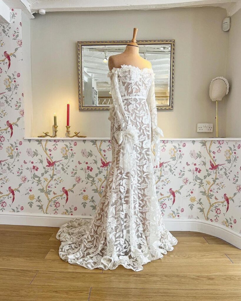 White lace wedding dress with leaf patterns on a mannequin in floral room
