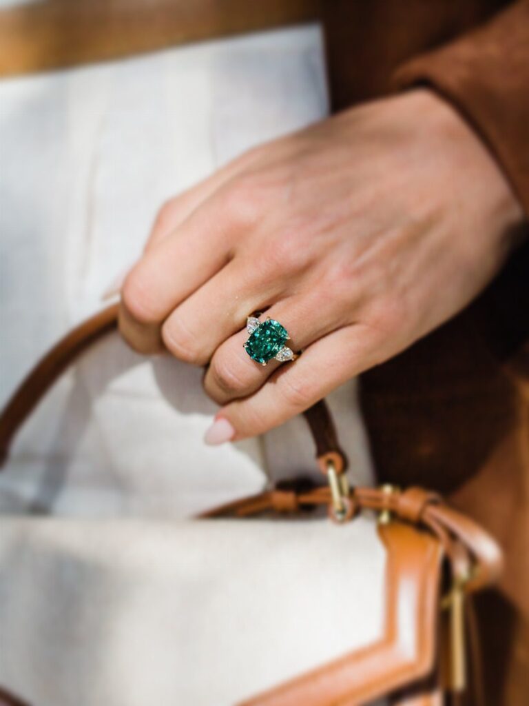 Gold engagement ring with a large green gemstone and diamonds on a finger