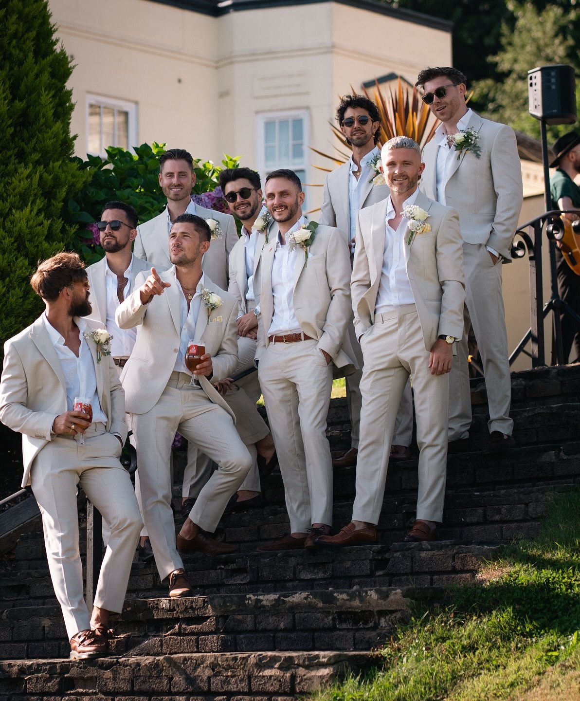 Group of groomsmen wearing matching light beige casual suits on stone steps outdoors.