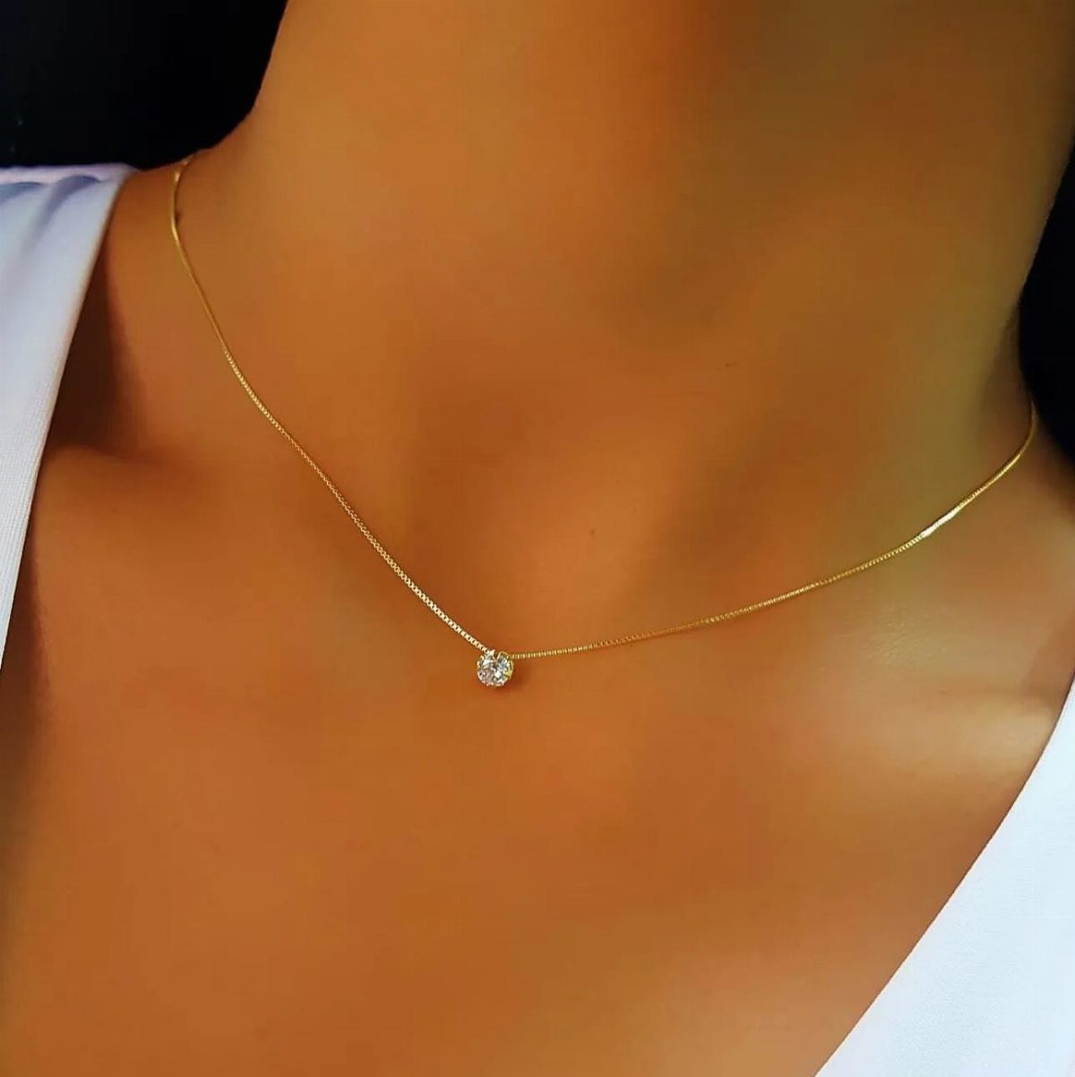 Thin gold chain necklace with a small diamond pendant on a strapless white dress