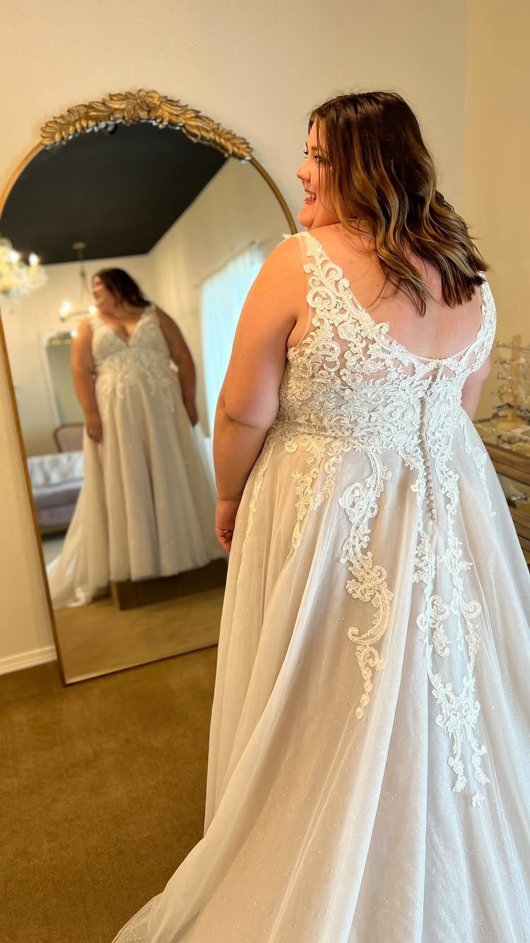 Woman in a white sparkly lace wedding dress posing before an oval mirror.