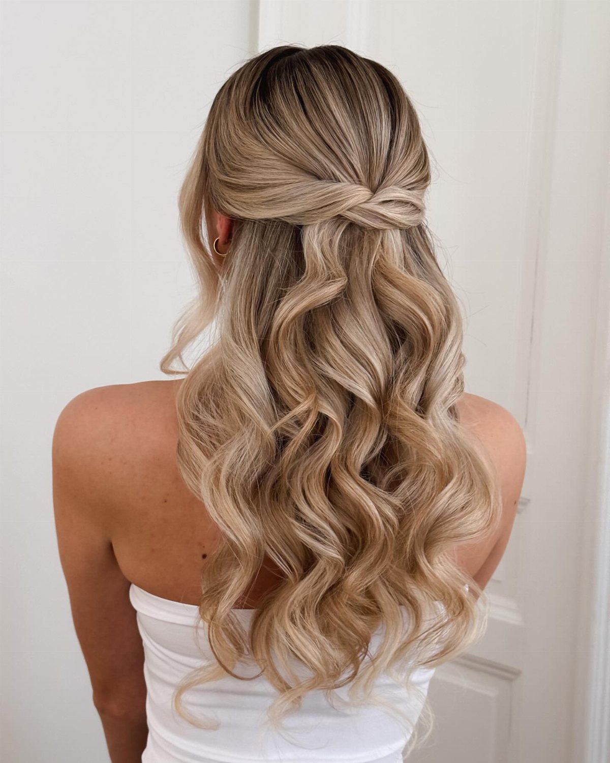 Blonde wavy hair styled in a half-up half-down twist with cascading curls.