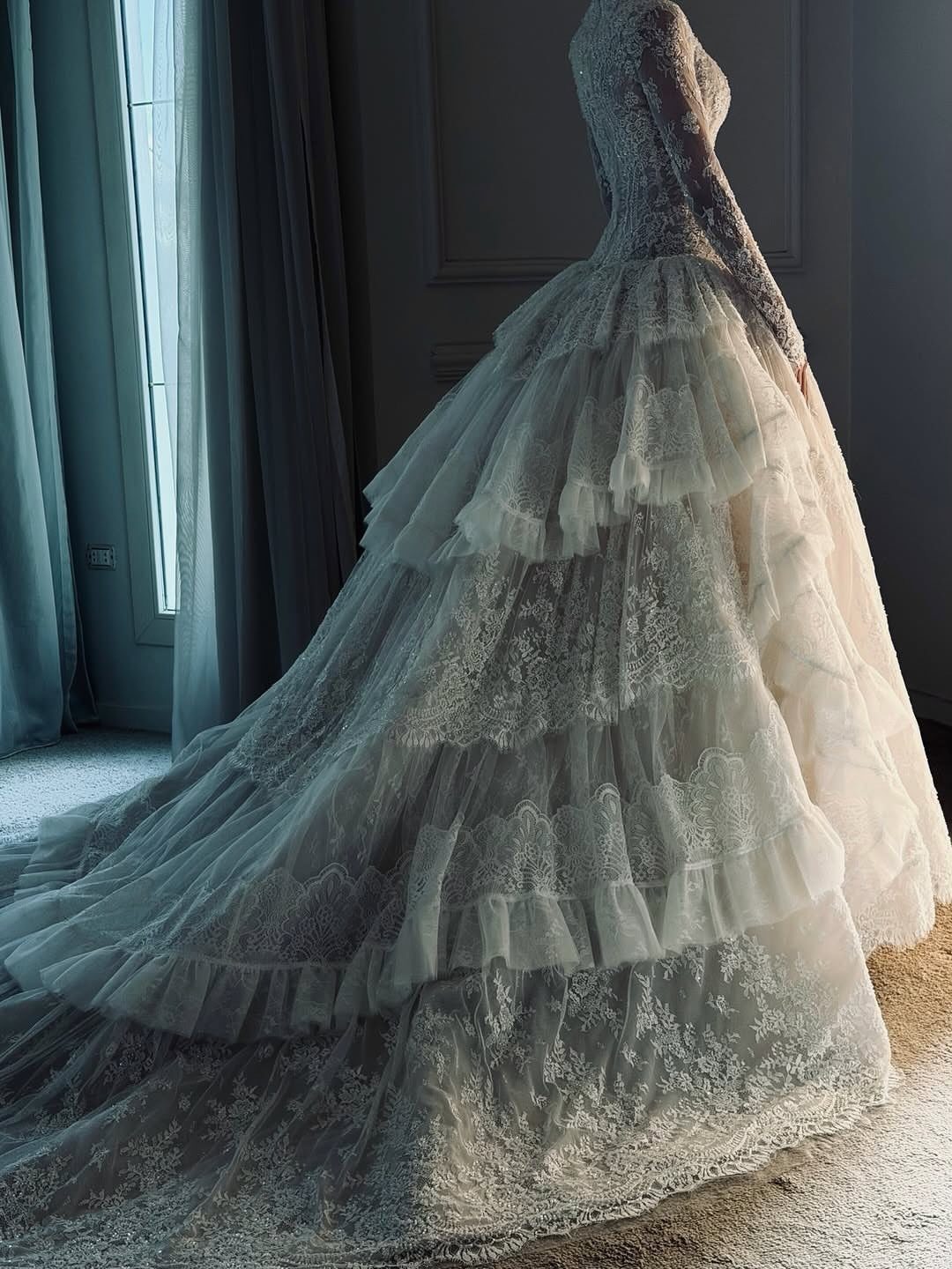 Tiered white lace wedding dress with a long train in a soft-lit room