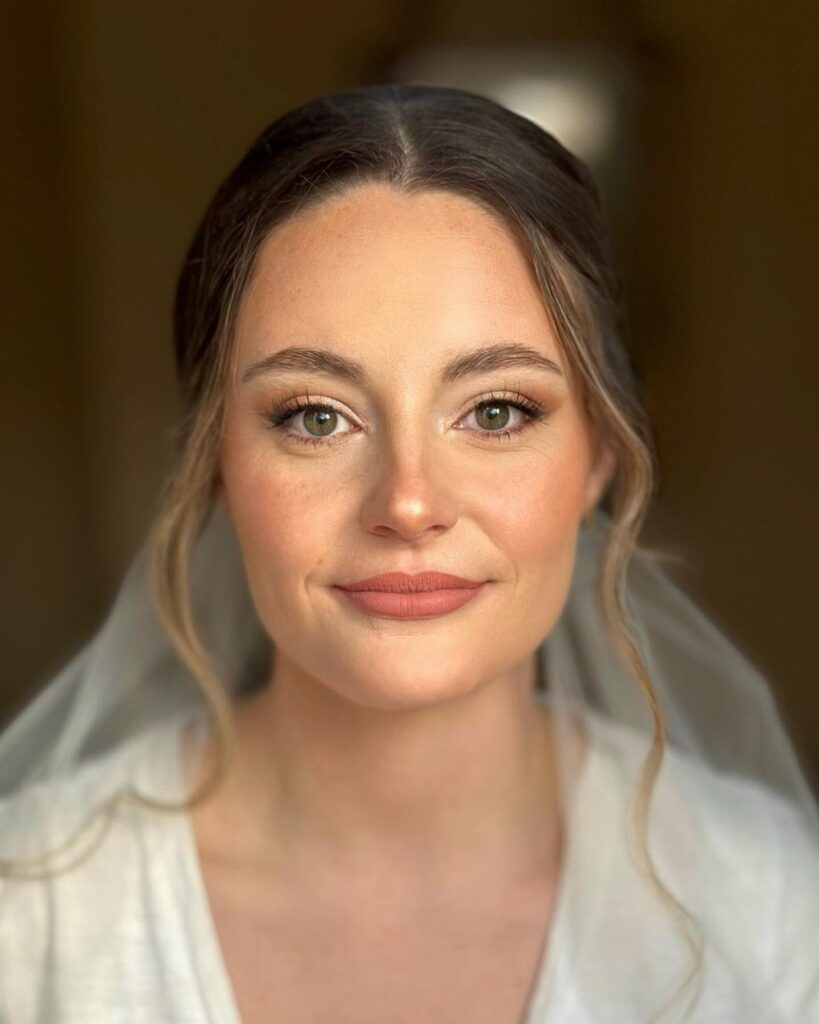 Bride with peachy monochromatic makeup, wearing a white veil and white top.