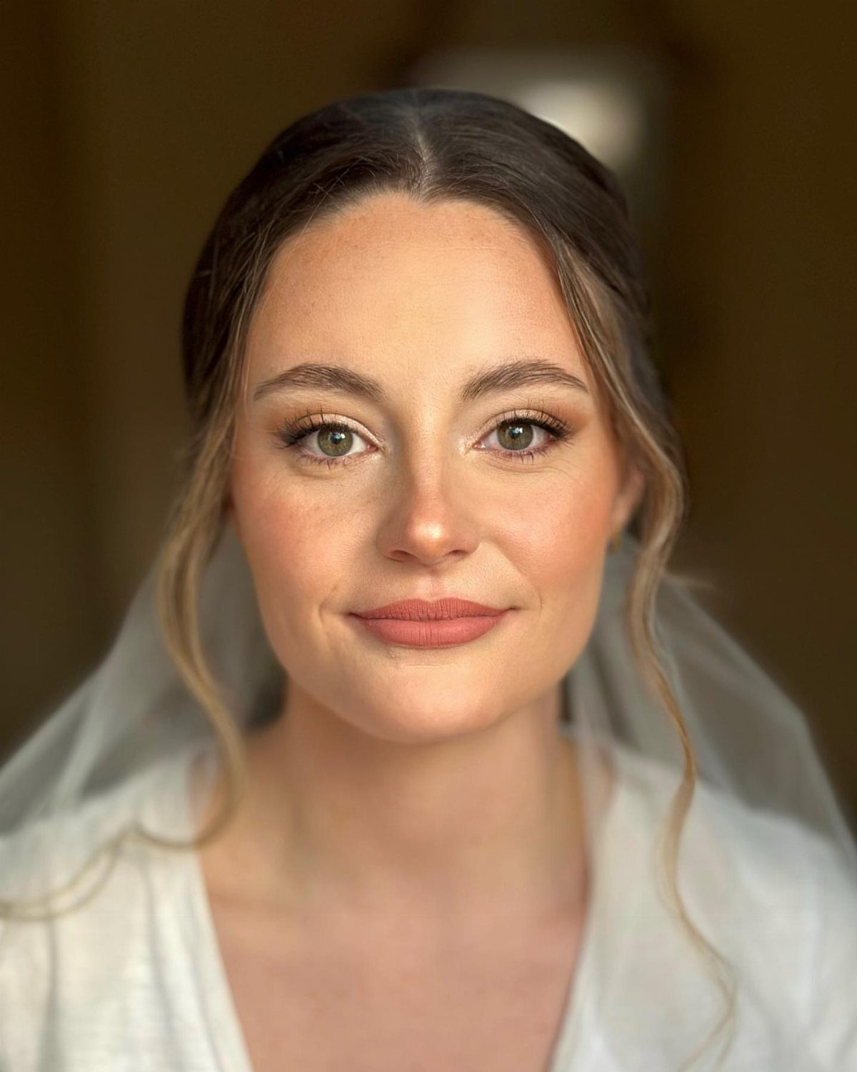 Bride with peachy monochromatic makeup, wearing a white veil and white top.