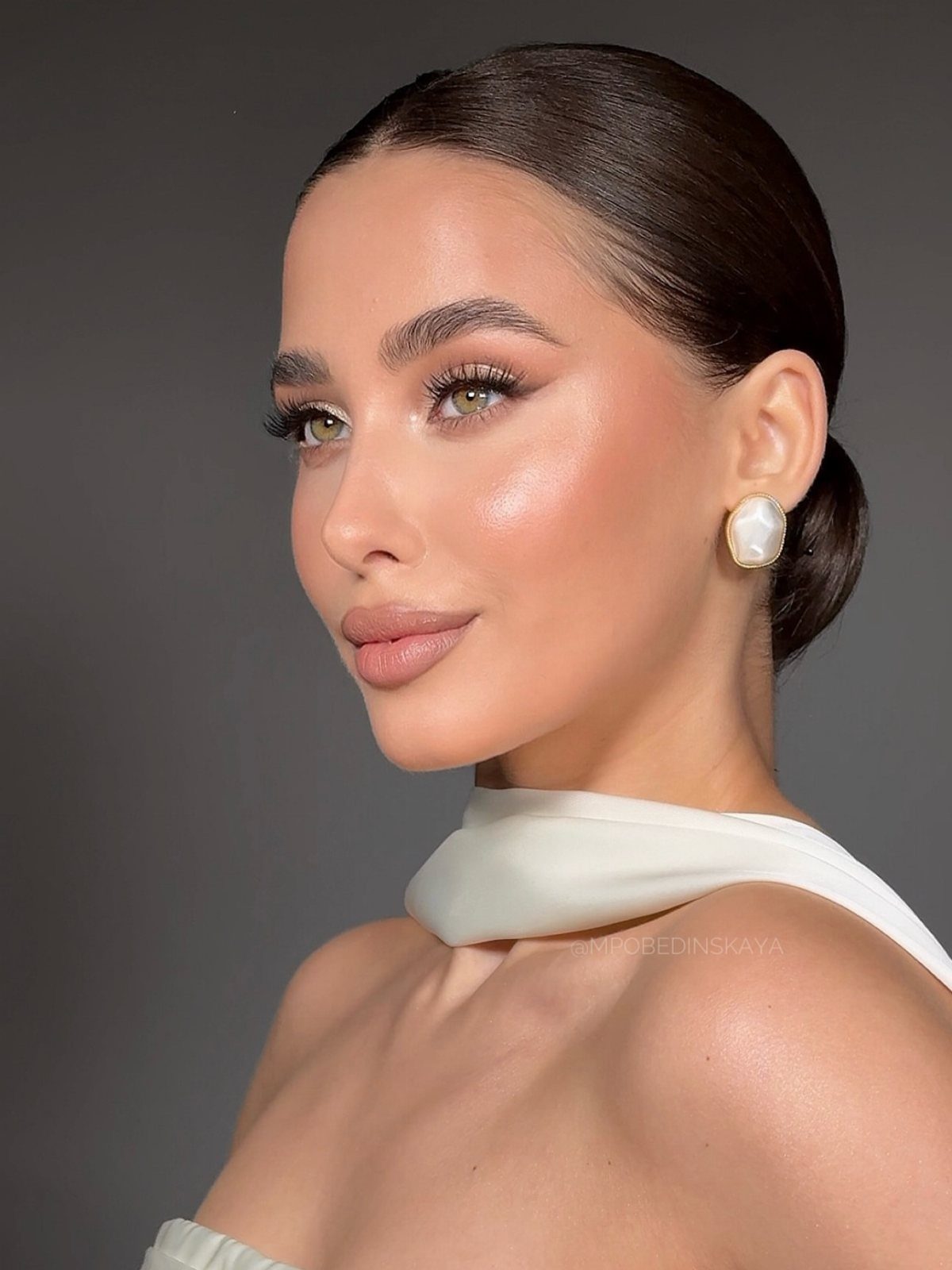 Woman with soft glam bridal makeup, sleek bun, and white halter top.