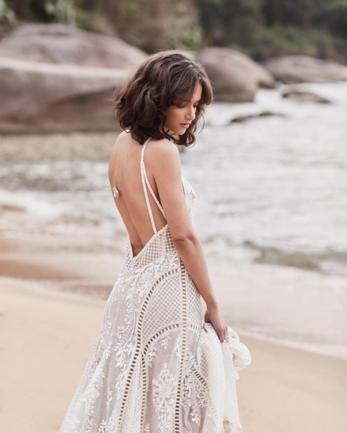 Woman in a white lace wedding gown standing on a sandy beach