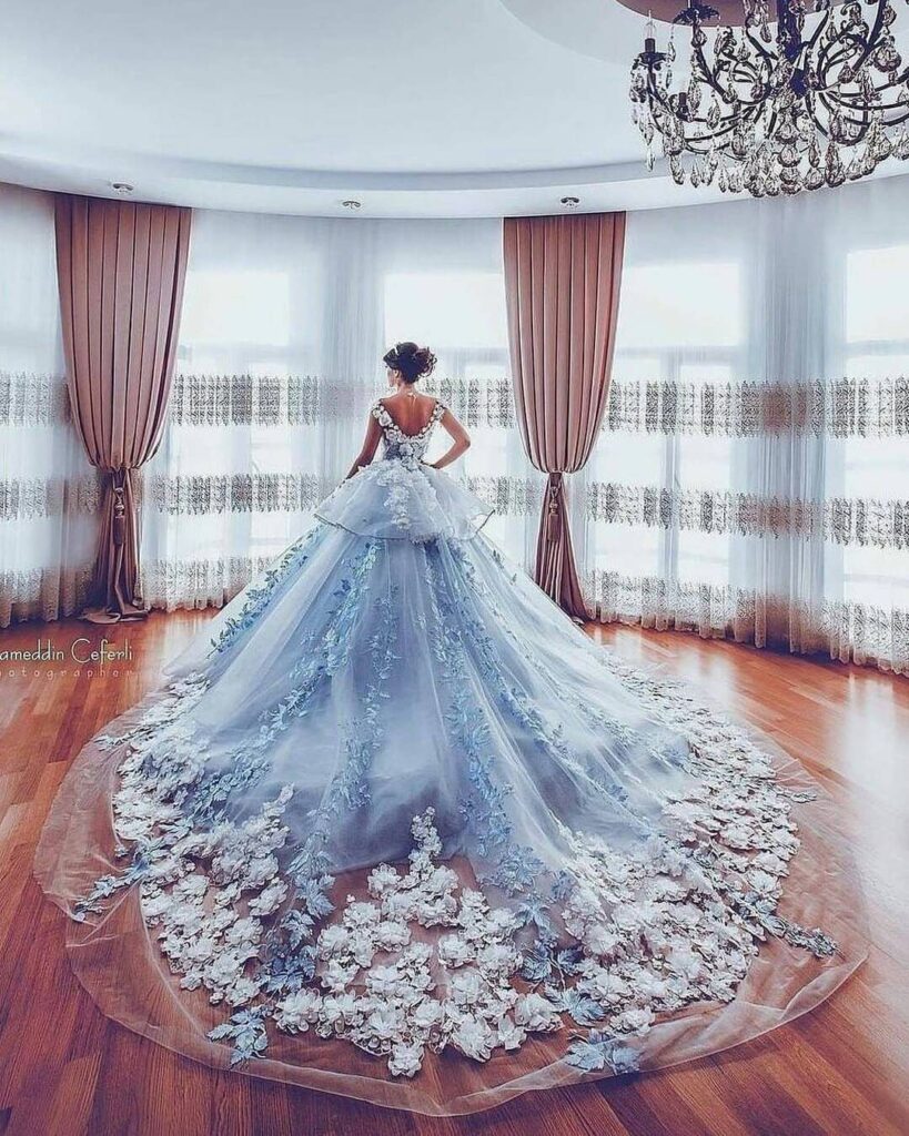 Woman wearing a voluminous light blue wedding dress with floral lace in a room.