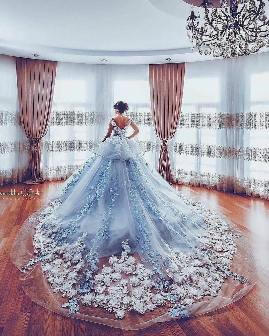 Woman wearing a voluminous light blue wedding dress with floral lace in a room.