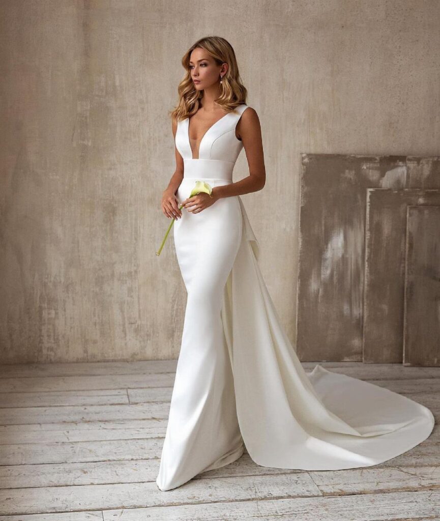 Woman in a simple elegant white wedding dress holding a yellow calla lily
