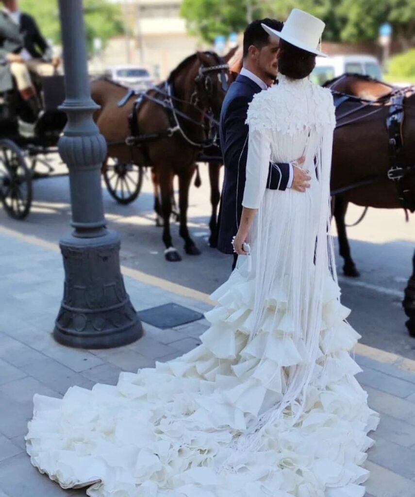Woman in white flamenco style wedding dress with ruffles and fringe embracing a man.