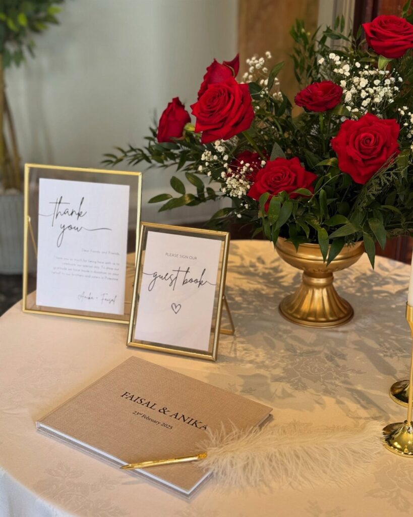 Wedding guest book table with red roses, gold frames, and a brown book.