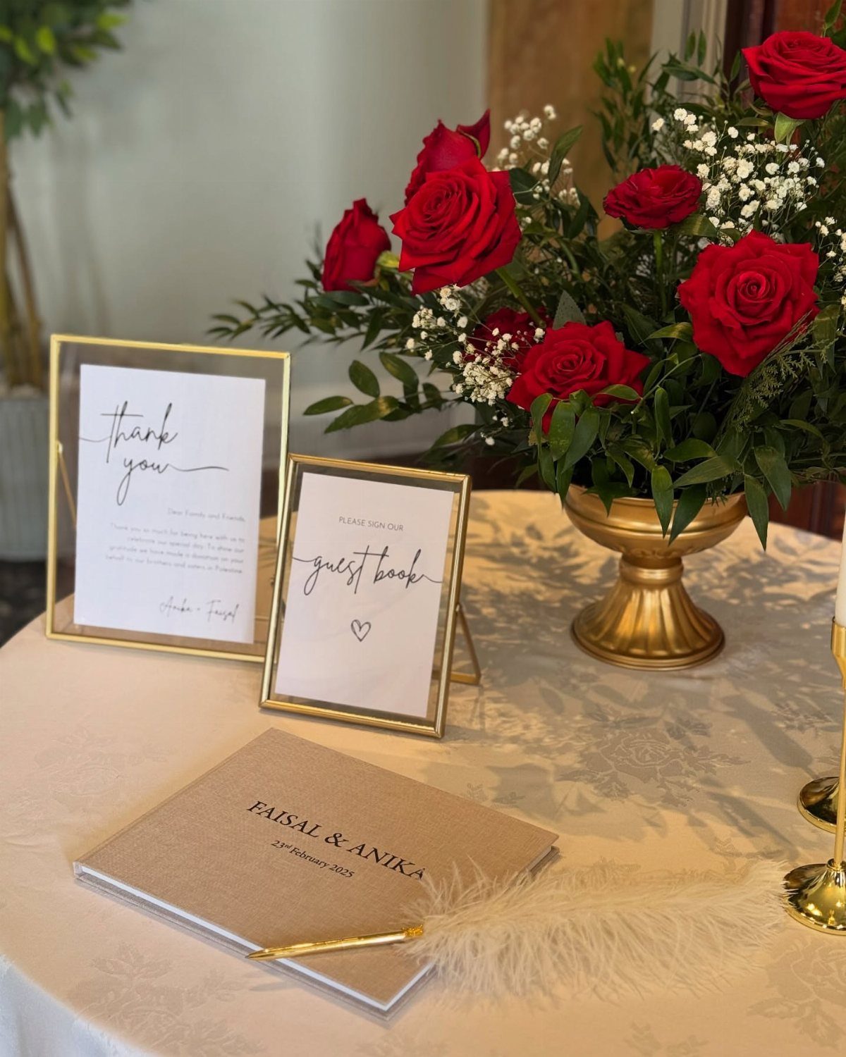 Wedding guest book table with red roses, gold frames, and a brown book.