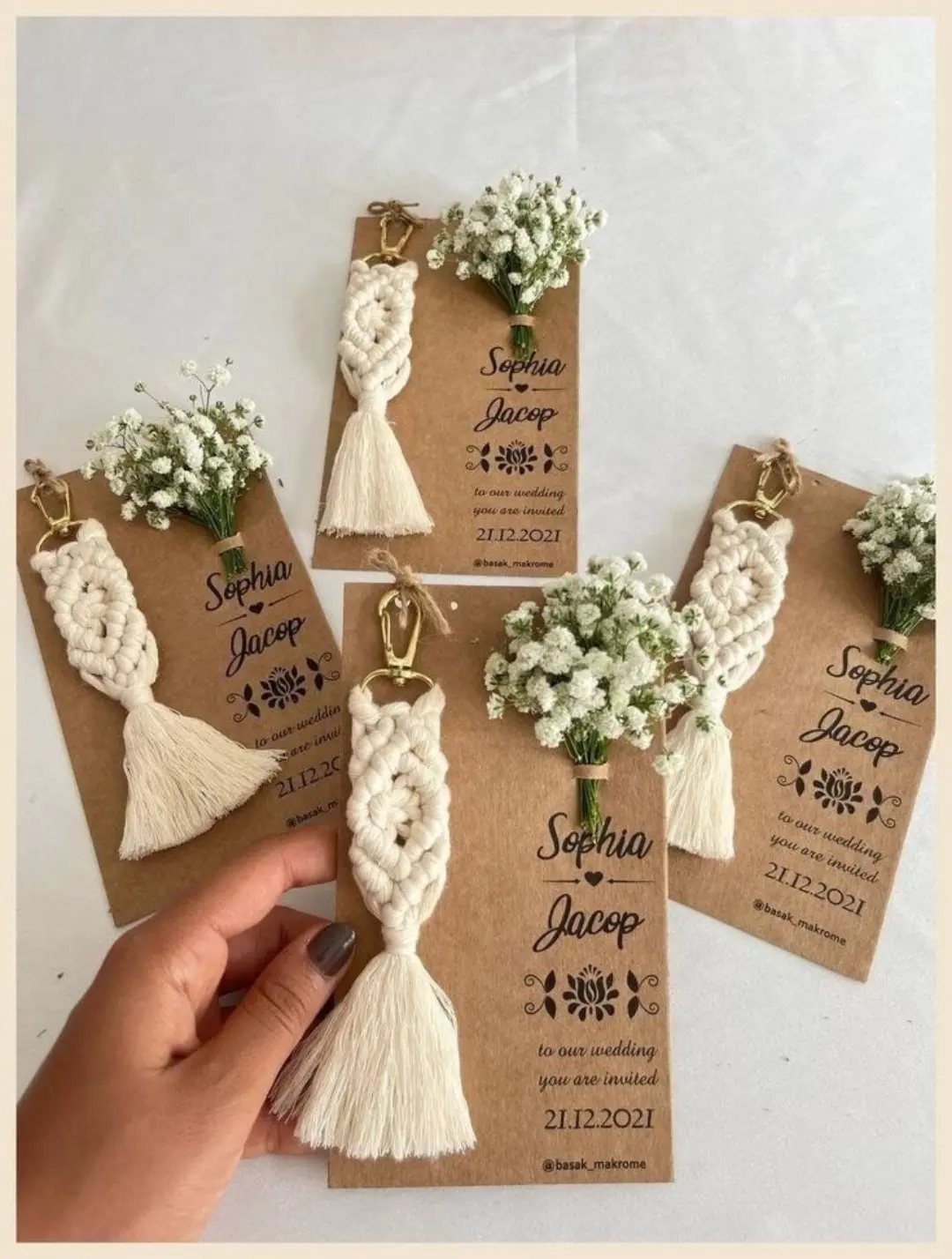 Macrame tassel keychains and baby's breath flowers attached to brown wedding invitation cards.