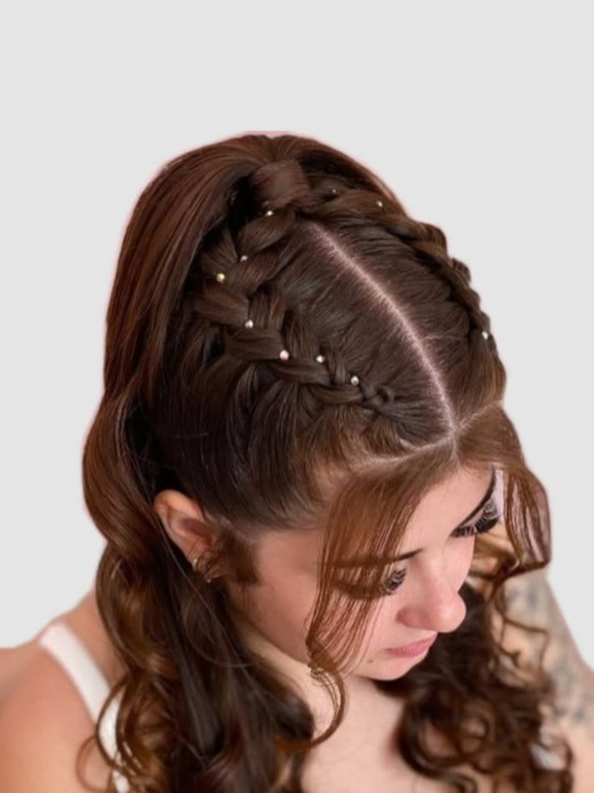 Woman with long brown curly hair in a braided ponytail with pearl accents