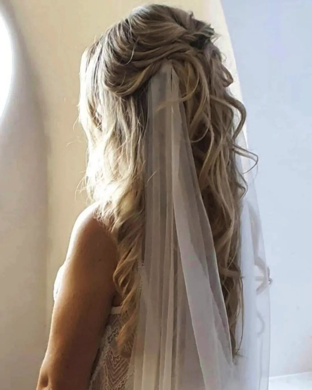 Blonde hair in loose waves with a half-updo and long white cathedral veil
