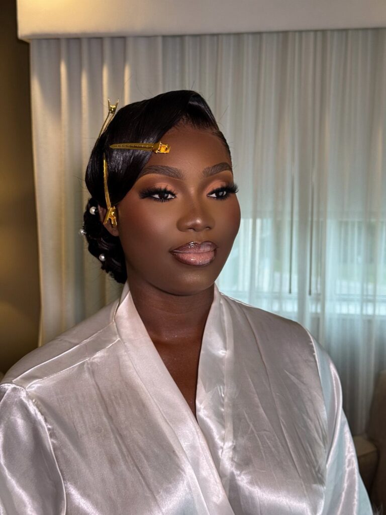 Woman with dark skin wearing bridal makeup and a white satin robe