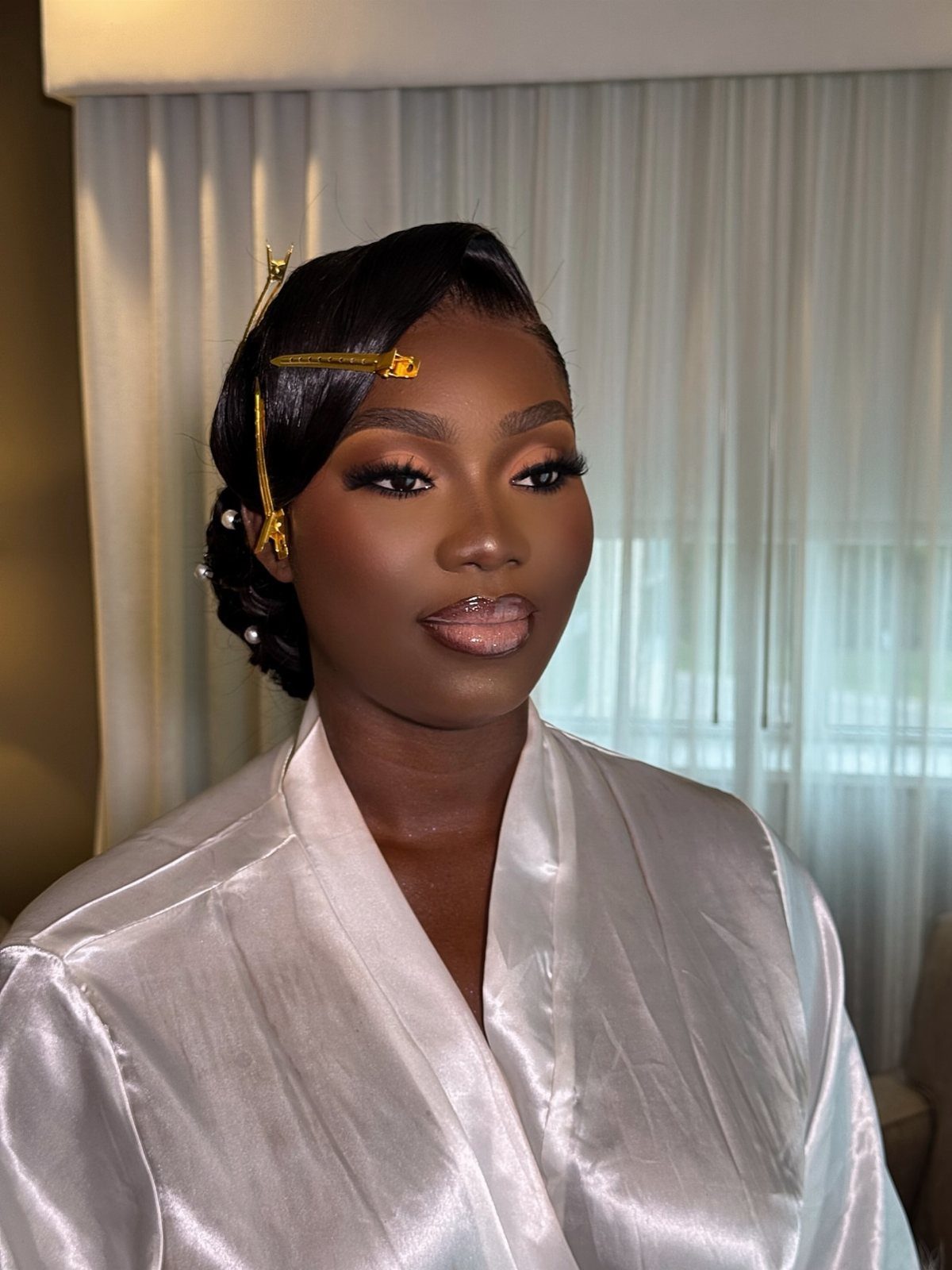 Woman with dark skin wearing bridal makeup and a white satin robe