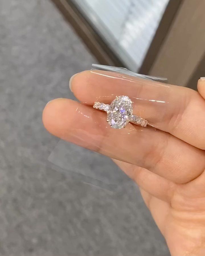 Oval-cut diamond wedding ring with side stones held between two fingers.