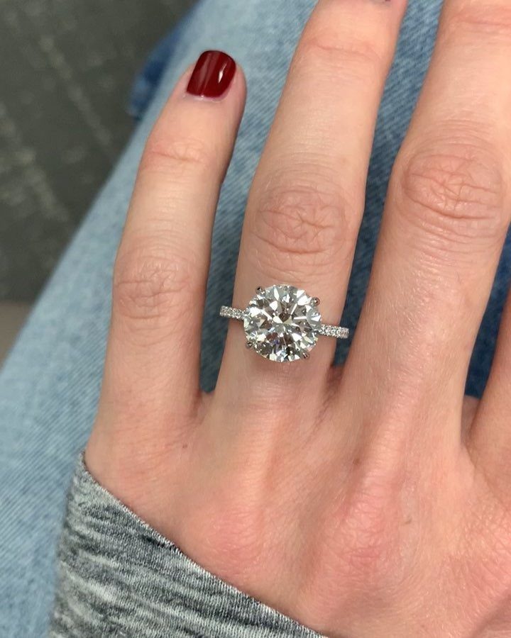 Large round-cut diamond ring on a finger with red nail polish